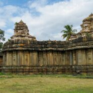 Ancient stone temple architecture surrounded by greenery under a cloudy sky, featuring intricately carved pillars